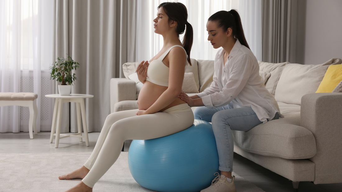 Picture: Pregnant woman sits on a birth ball with her doula behind her on a couch giving counter presser on her lower back