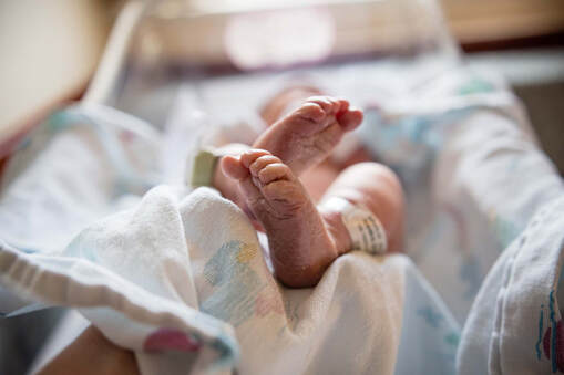 Picture of a baby in a hospital basinet covered with a hospital swaddle blanket. The picture is taken at an angle where all you can really see is the baby's feet.