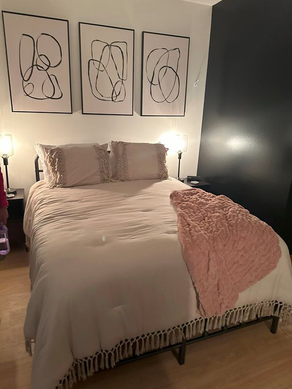 Ohio Birth Center bed with two night stands with lights on them with line art above it on a white wall with a black accent wall. The bed is comfy with white frilly pillows and a soft pink blanket draped over it.