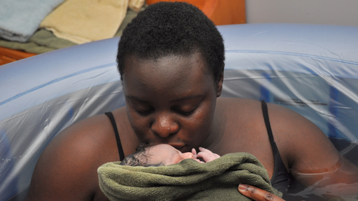 Picture of a black woman after having a home birth. She is in the birth pool holding and kissing her baby after her home birth.